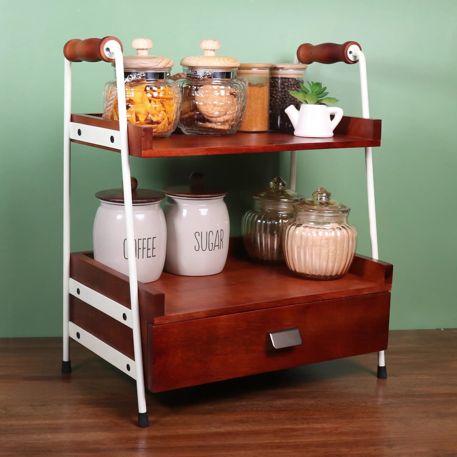 Loosebucket Two-tier wooden kitchen rack with storage jars against a green wall.