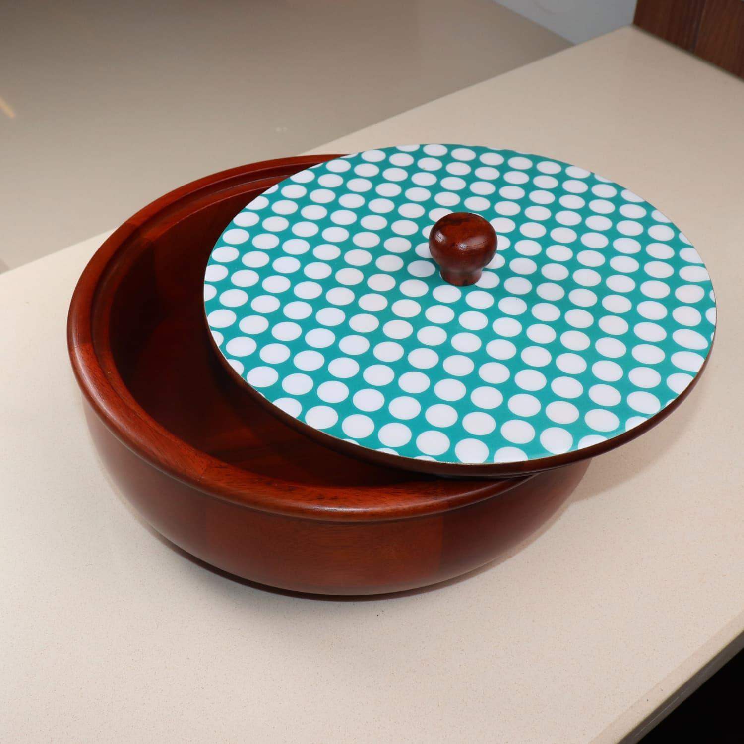 A LOOSEBUCKET The Dot legacy Chapati Box in India with a glossy finish sits on a light-colored countertop. The wooden bowl has a partially removed lid featuring a teal background with white polka dots and a wooden handle, revealing an empty interior.
