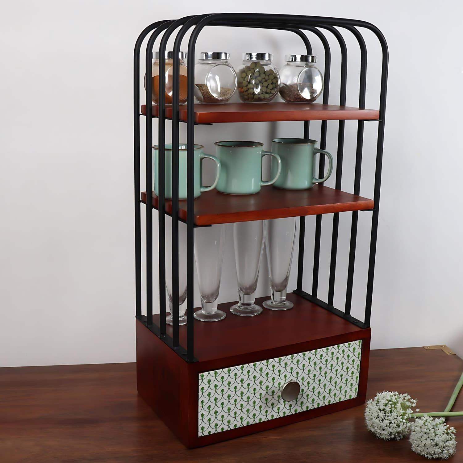 The Green bellezza Wooden Kitchen Organizer featuring three walnut brown shelves with black metal frame, displaying glass spice jars, mint green mugs, and tall glasses, complemented by a decorative patterned drawer at the base. Perfect for kitchen and living area storage and organization.