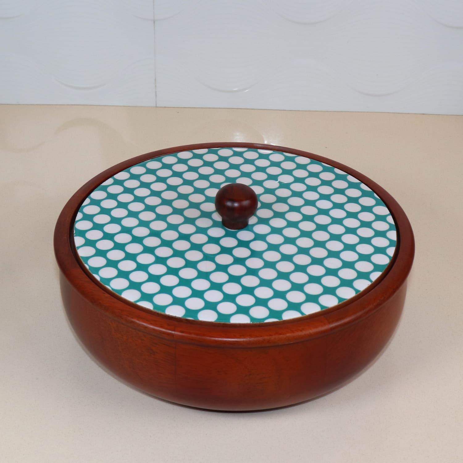 A round wooden container with a lid displaying a blue and white polka dot pattern. This charming The Dot legacy Chapati Box by LOOSEBUCKET sits on a light surface, and the lid features a small wooden knob for easy removal. The background is an off-white wall, making it easy to see why it's considered the best chapati box online in India.