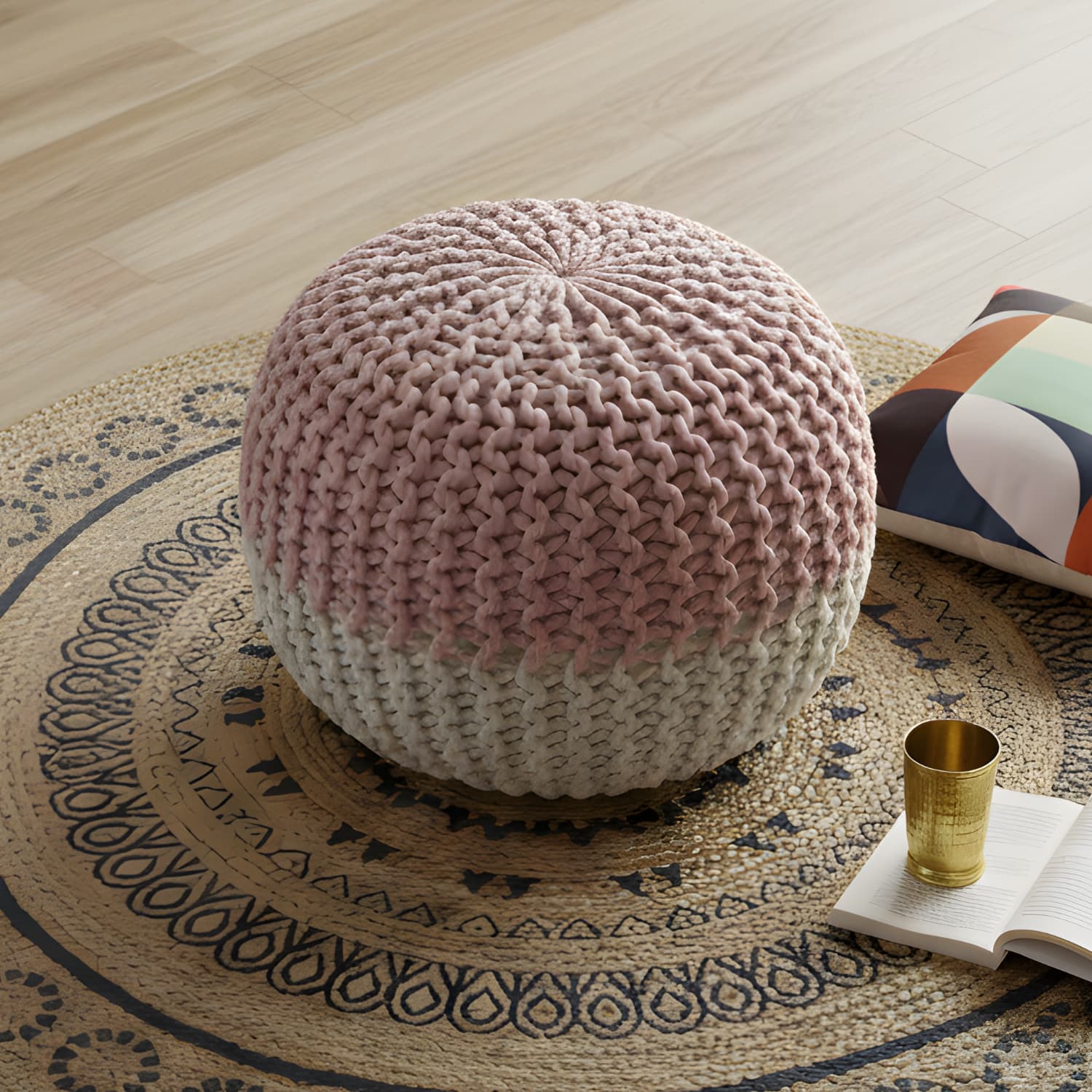 Loosebucket Knitted ottoman with gradient color on a patterned rug with a gold cup and book.