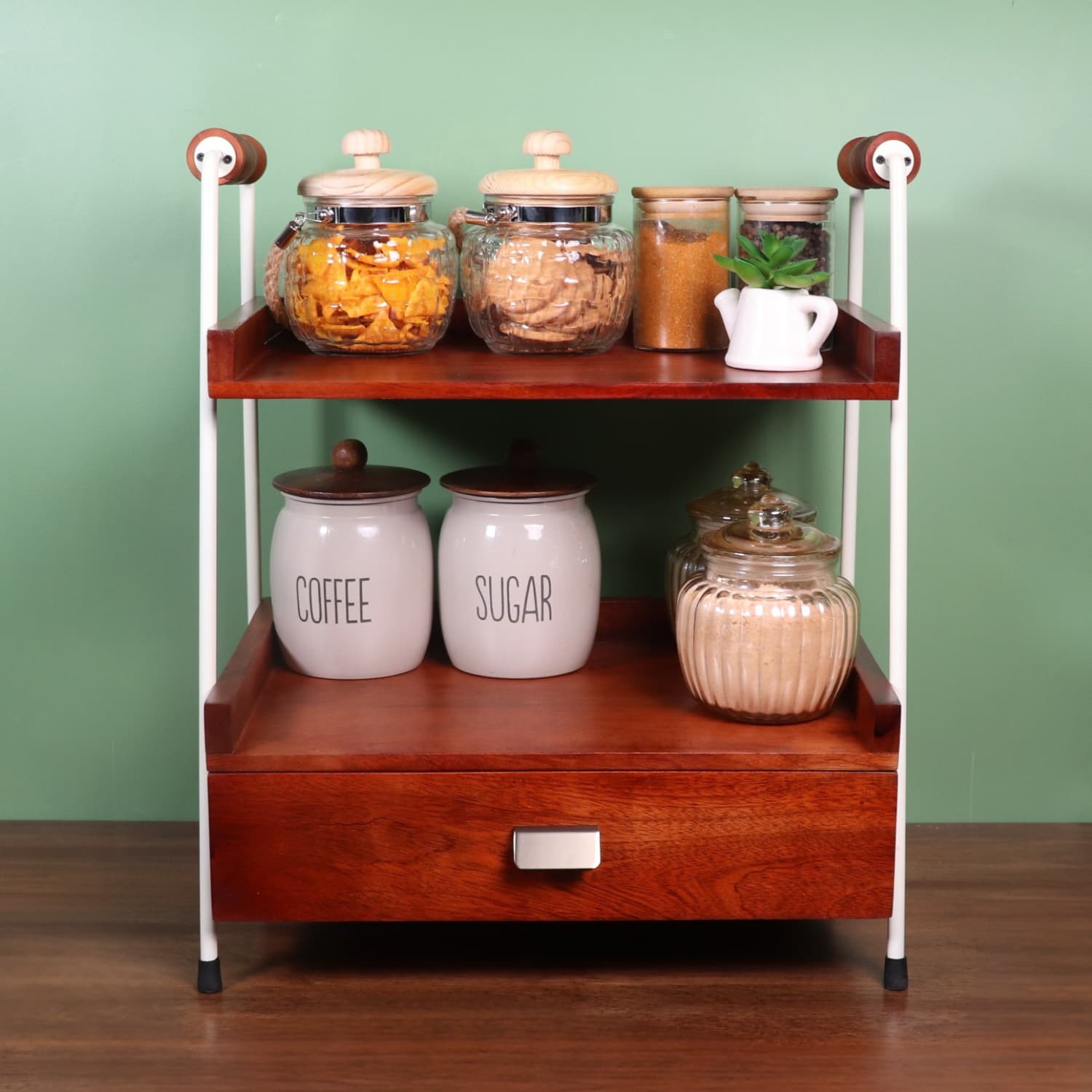 Loosebucket Wooden kitchen shelf with various jars and a drawer against a green wall.