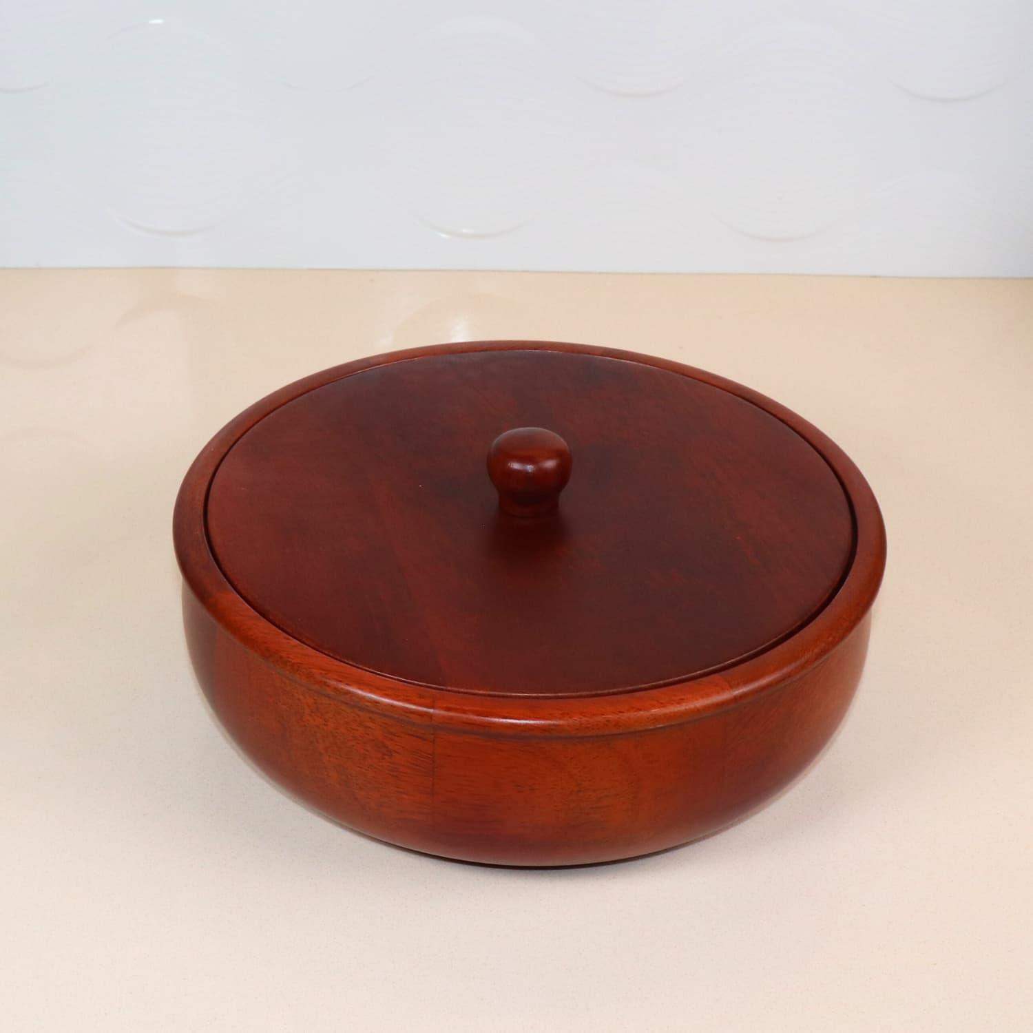 A round, polished wooden container with a matching lid and a small knob handle sits on a smooth, light-colored surface. This premium The Woody Casserole Chapati box by LOOSEBUCKET in India has a rich, dark brown finish, highlighting its natural wood grain.
