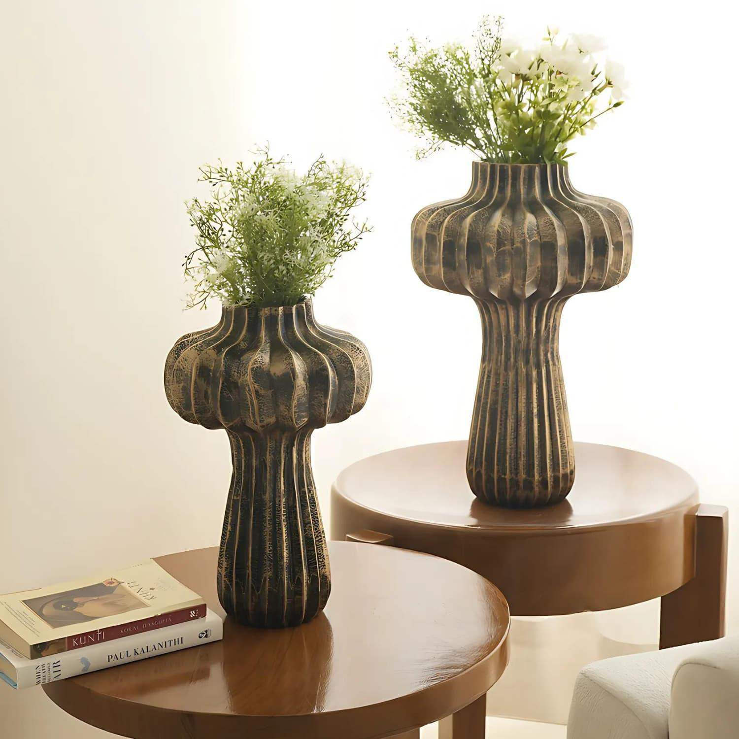 Premium Vintage Portobello Aluminum Vases displayed on round wooden tables, featuring two mushroom-shaped vases in antique golden brown finish with ribbed texture, holding delicate white and green floral arrangements. Taller vase measures 16 inches, shorter 12 inches.